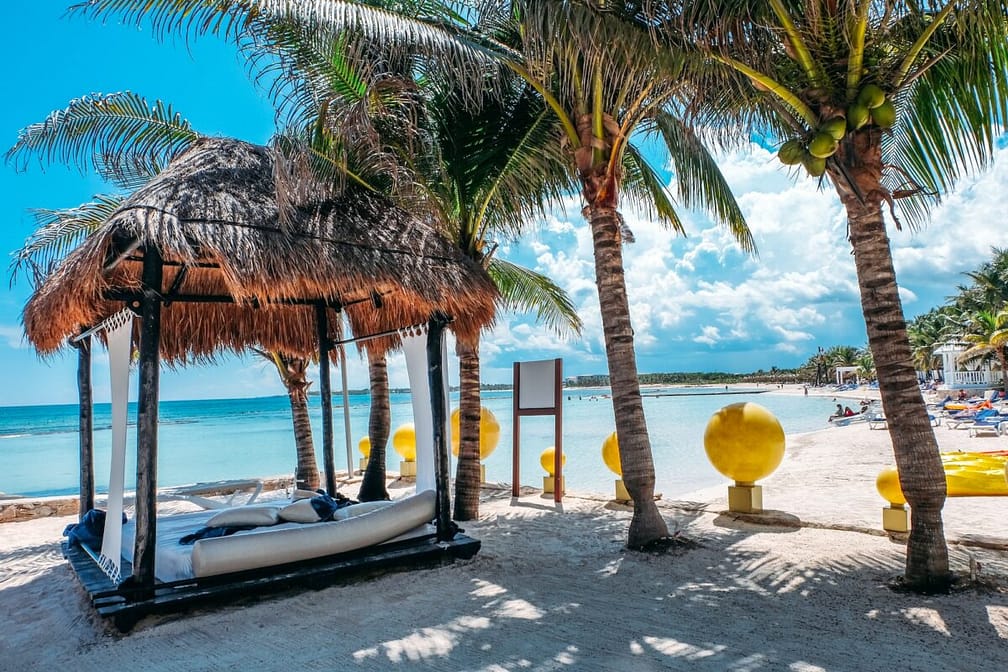 Bali bed on tropical white sandy beach, blue ocean with palm trees. Paradise in Mexico