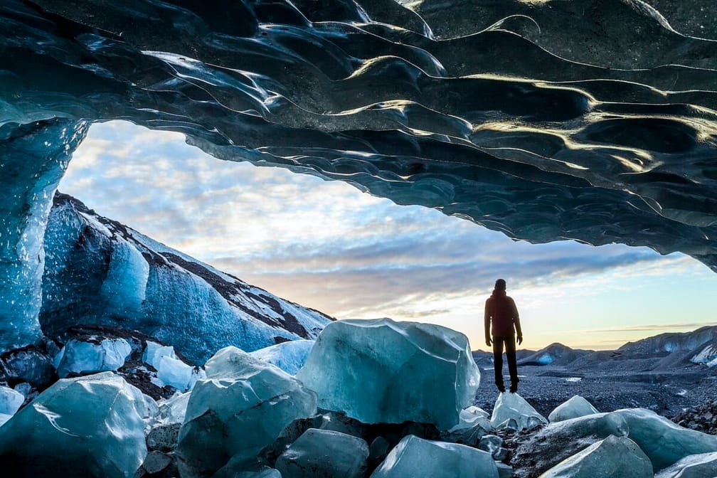 Rear view silhouette of person standing on ice rock at the entrance to a glacial ice cave.