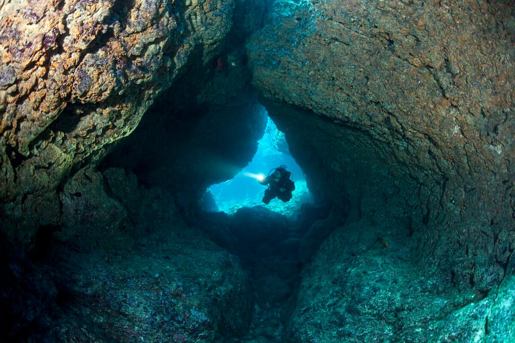 Scuba Diver with LIght Enters Coral Cavern