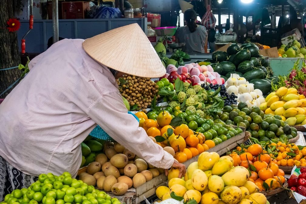 Vendor at his fruit and vegetable stall at a market in Hoi An, Vietnam.