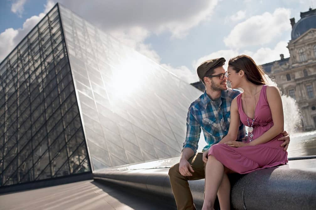 A couple sitting by the fountain by the glass entrance to the Louvre museum, Paris.