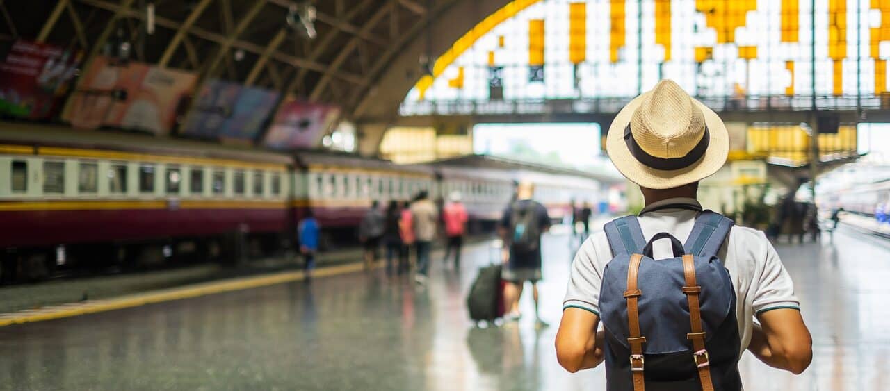 man traveler with backpack waiting for train, backpacker standing on railway platform at Bangkok