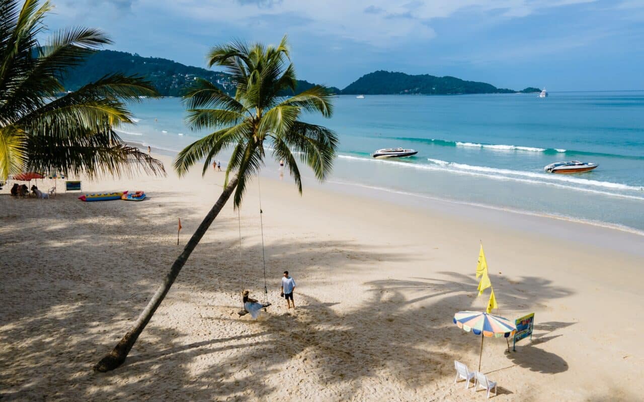 A couple of men and women on a swing under a palm tree at the beach of Patong Phuket Thailand