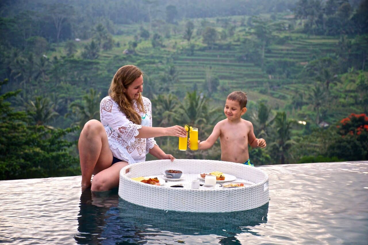 Young woman and a little boy are having breakfast in the infinity pool