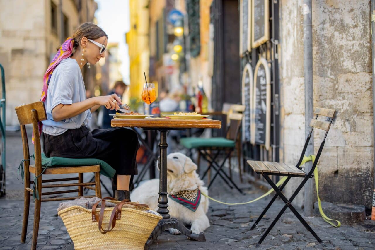 Woman eating italian pasta while sitting with a dog at restaurant on the street in Rome