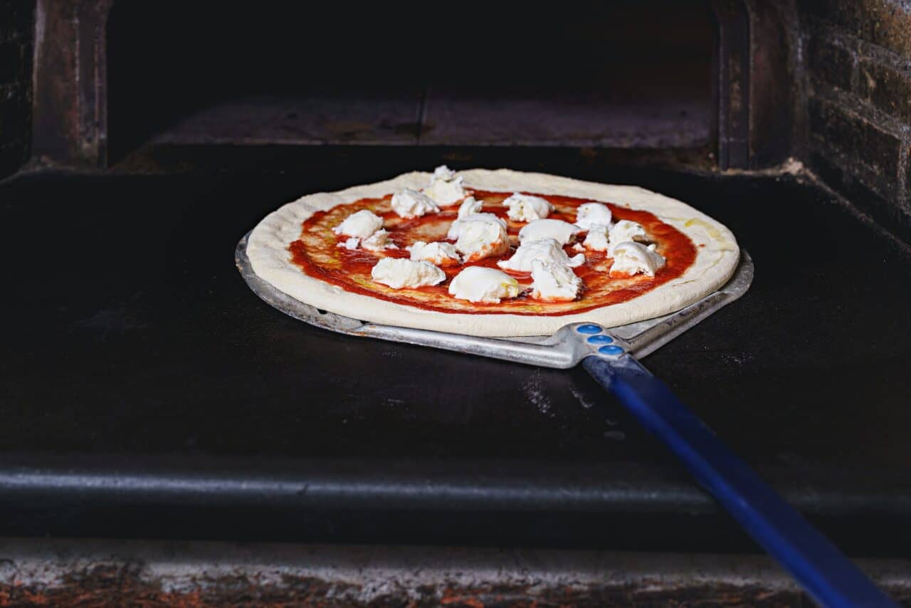 The pizza maker inserts a traditional margherita pizza in the stone oven